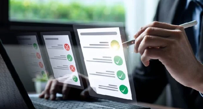 Person reviewing assessment sheets with green check marks and red Xs on a laptop screen with a stylus in hand.