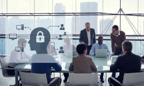 Business meeting in a glass-walled office with an overlay of a head silhouette and a padlock, signaling cybersecurity.