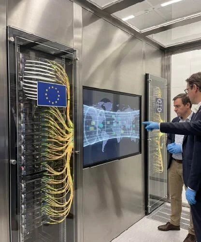 Two men in a data center inspect server racks with an EU flag on the cabinet and a glowing world-map display between them.
