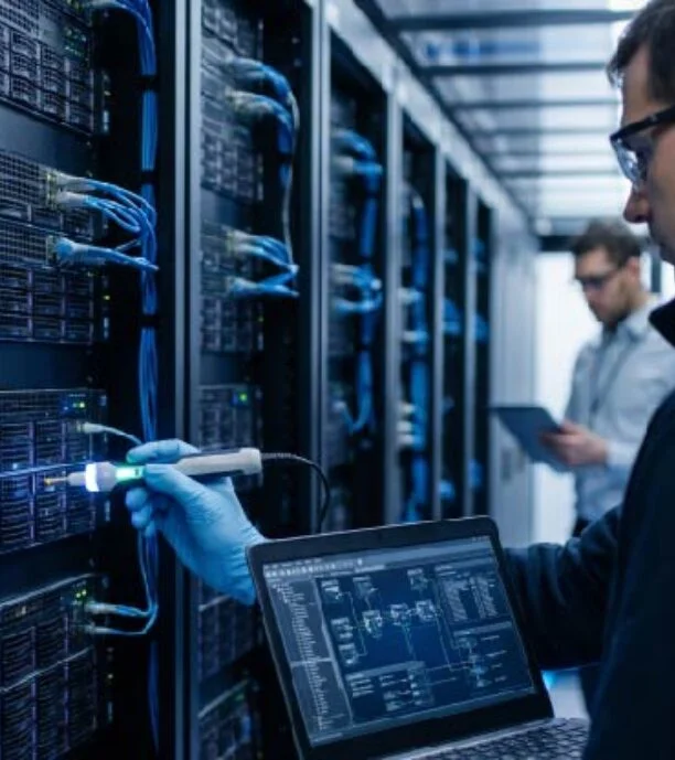 Network technician checks server rack with a handheld tester while laptop shows a diagram in a data center.