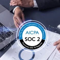AICPA SOC 2 badge centered on a desk with hands, laptop, and documents, signaling trusted security controls.