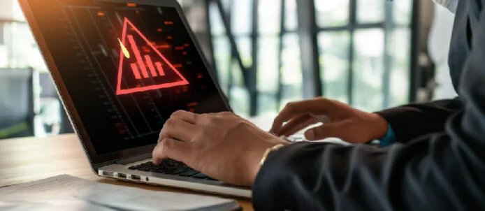 Person in a suit typing on a laptop that shows a red warning triangle and data graphs, signaling a cybersecurity alert.