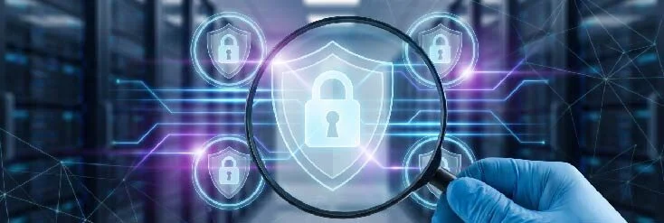 Blue-gloved hand holds a magnifying glass over a glowing shield-shaped padlock, symbolizing cybersecurity and data protection.