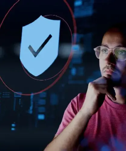 A person wearing glasses contemplates cybersecurity, with a shield and checkmark symbol representing protection in a tech interface.