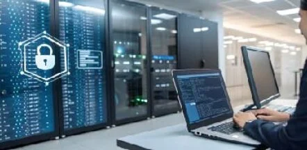 Person typing on a laptop beside server racks in a data center, with a glowing security hexagon icon atop the scene.
